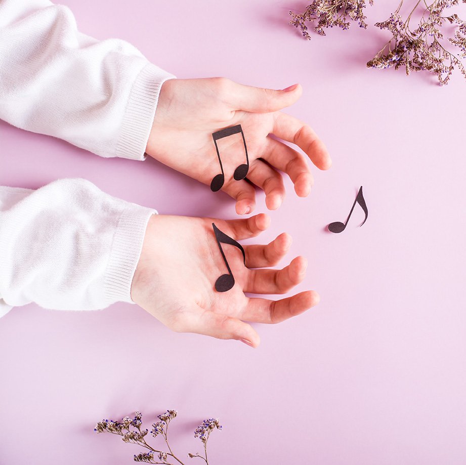 Children's hands hold paper notes on a pink background. Music ed